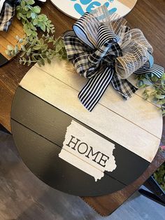 a wooden sign that says home with a bow on it and some plants in the background