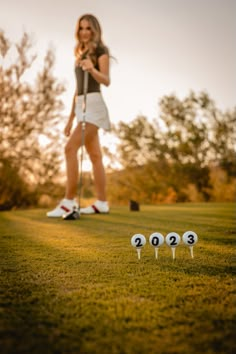 a woman standing on top of a lush green field next to three white golf balls