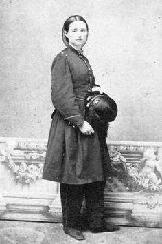 an old black and white photo of a woman with a hat on her head standing in front of a wall