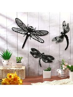 three dragonflys are mounted to the side of a white wooden wall with potted plants