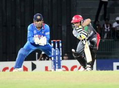 two men playing cricket on a field with spectators in the background