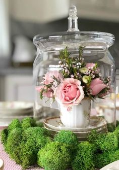 there is a glass jar with flowers in it and moss on the table next to candles