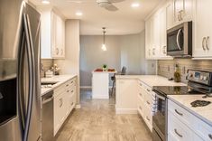 a kitchen with stainless steel appliances and white cabinetry, along with marble counter tops