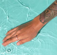 a person's hand with a tattoo on it sitting in the water next to a swimming pool