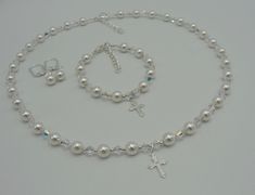 "This beautiful First Holy Communion necklace and bracelet set is now offered with an elegant pair of Swarovski Pearl and Crystal earrings that will definitely add to your beautiful day. This set is designed using 6mm Swarovski Pearls and 4mm Swarovski Crystals. The cross is sterling silver with a cubic zirconia. The bracelet measures 6\" and has a 1\" extender chain. The necklace measures 16\" with a 1 1/2\" extender chain. The coordinating pair of earrings are designed using a 6mm Swarovski Pe Elegant Pearl Jewelry For Confirmation, Elegant Round Jewelry For Baptism, Elegant Pearl White Jewelry For Baptism, Elegant Pearl Jewelry For Baptism, Elegant Silver Jewelry For Confirmation, Elegant Sterling Silver Jewelry For First Communion, Silver Round Beads Jewelry For First Communion, Elegant Pearl White Jewelry For First Communion, Elegant Personalized Jewelry For Confirmation