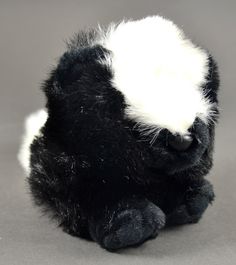 a black and white stuffed animal sitting on top of a gray floor next to a wall