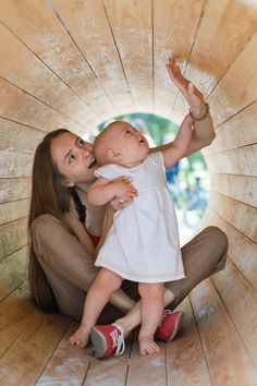 a woman holding a baby in her arms while sitting on the floor inside a wooden structure