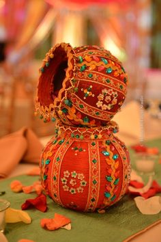 an orange vase with green and red beads on it's sides sitting on a table