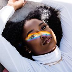 a woman laying on the ground with her hands behind her head and rainbow painted on her face