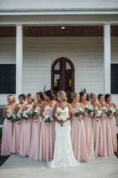 a group of bridesmaids standing in front of a white house with their bouquets