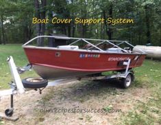 a red boat sitting on top of a trailer in the grass next to some trees