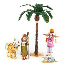 three figurines are standing next to a palm tree and an animal on the ground