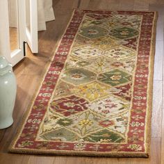 a red and green rug on the floor next to a blue vase with flowers in it