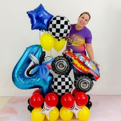 a woman standing next to balloons and an inflatable number six monster truck on the floor