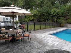 an outdoor table with chairs and umbrella next to a swimming pool in a backyard area