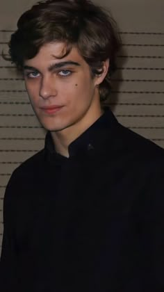 a young man with dark hair and blue eyes wearing a black shirt looking at the camera