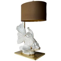 a white fish lamp on a gold base with a brown lampshade over it