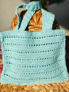 a blue crocheted bag sitting on top of a woven straw basket next to a plant