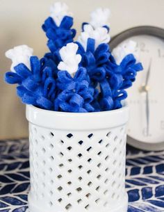 blue and white flowers are in a white vase on a table next to a clock