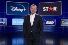 a man in a suit and tie standing next to three disney logos on the wall