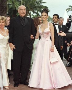 an older man and woman in formal wear walking down the red carpet at a ceremony