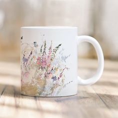 a white coffee mug sitting on top of a wooden table covered in lots of flowers