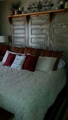 a bed with white sheets and red pillows in a bedroom next to two wooden shutters