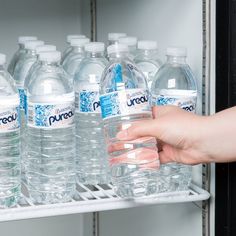 a hand reaching for a bottle of water from an open refrigerated refrigerator