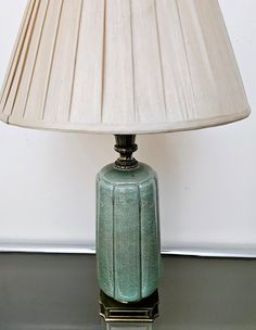 a green lamp sitting on top of a table next to a white wall and floor