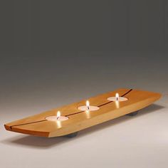 three candles are placed on top of a wooden surfboard that is shaped like a boat