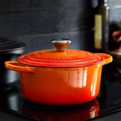 an orange casserole dish sitting on top of a black stove with a bottle in the background