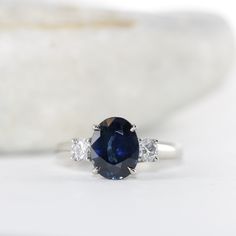 a blue sapphire and diamond ring on a white surface with a stone in the background