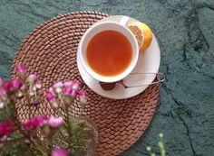 a cup of tea on a wicker place mat next to some flowers and lemon slices