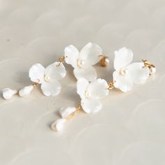 three white flowers with pearls hanging from them on a gold plated earring chain