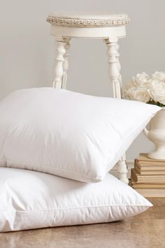 two pillows sitting on top of each other next to a white chair and vase with flowers