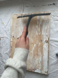 a person holding a pair of scissors in front of a piece of wood with paint on it