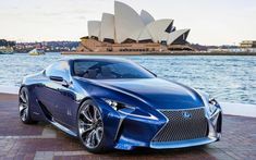 a blue sports car parked in front of the sydney opera house with water behind it