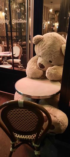 a large teddy bear sitting on top of a table next to a chair and window