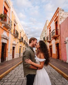 a man and woman standing next to each other in an alleyway with colorful buildings