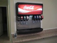 a coca - cola machine sitting on top of a counter next to a wall mounted tv