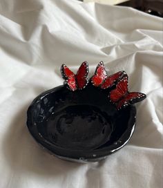 a black bowl with red butterflies in it on a white cloth covered tablecloth,