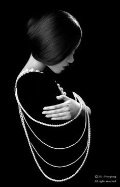 a woman with pearls on her neck wearing a black dress and holding onto a chain