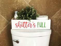 a toilet with a sign that says shitter's full on the lid and plants in it