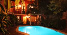 an outdoor swimming pool at night with lights on and plants in the yard around it