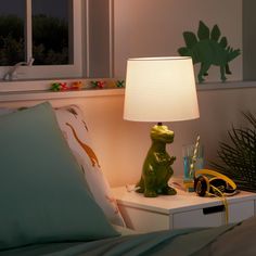 a dinosaur lamp sitting on top of a night stand next to a bed with pillows