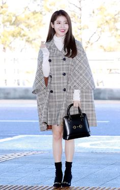 a woman in a plaid coat holding a black handbag and posing for the camera