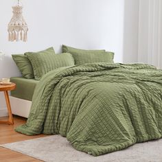 a bed with green comforter and pillows in a room next to a white wall