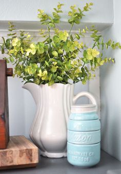 a white vase filled with yellow flowers next to a blue mason jar