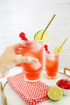 a person holding a glass with some fruit in it and two glasses on the table