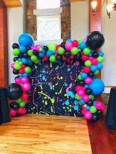 an arch made out of balloons in the middle of a room with black tablecloths